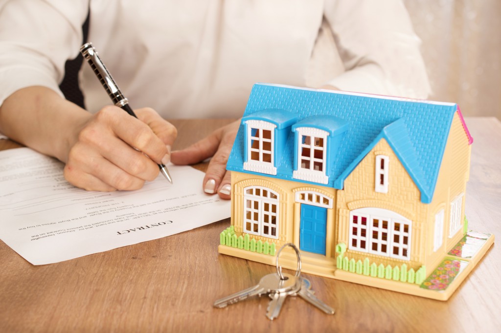 business, real estate, deal and people concept - man and woman with house model and pen signing contract document and shaking hands at office