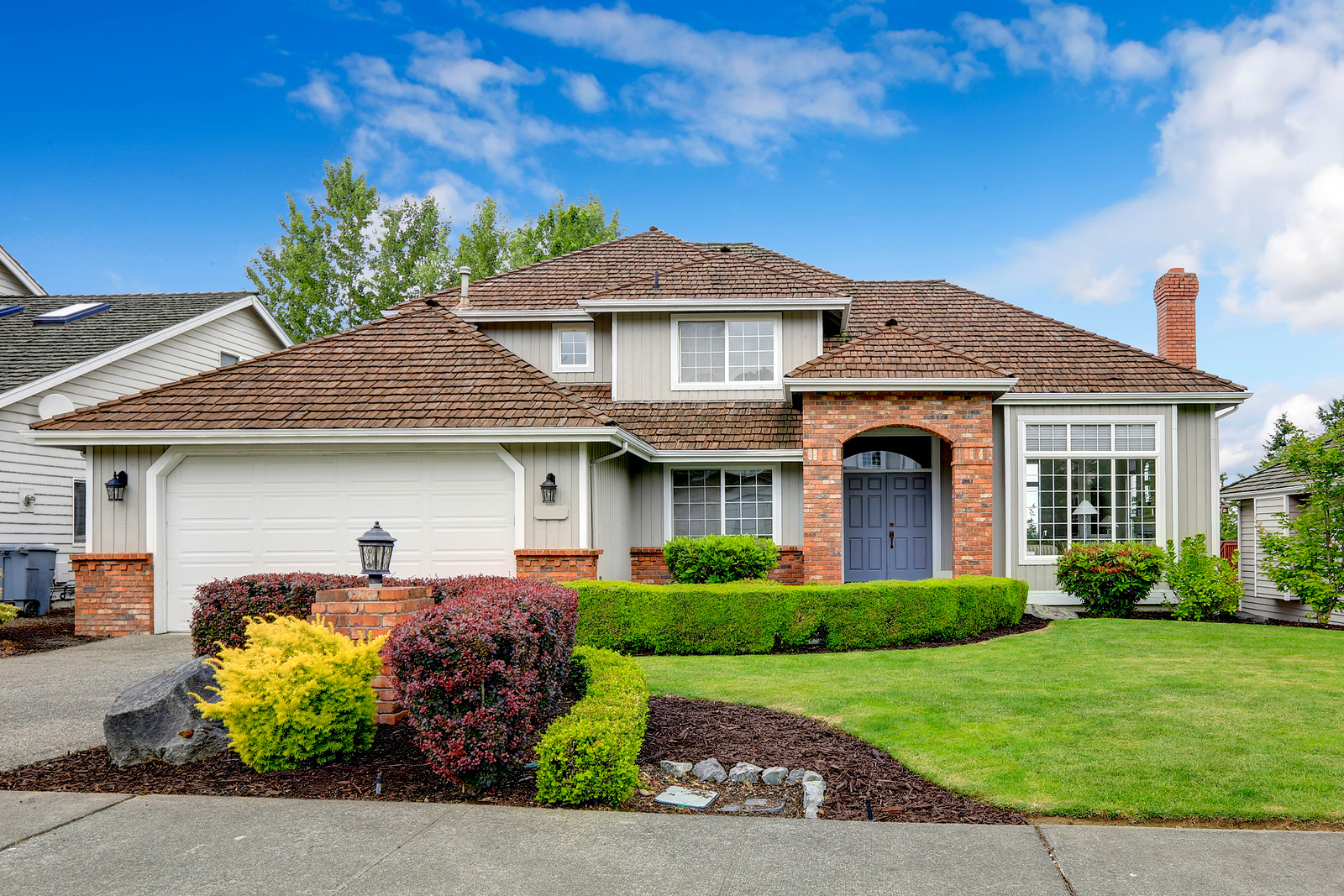 American House Exterior With Curb Appeal Classic house exterior with brick trimmed entrance porch green lawn and trimmed hedges. Garage with driveway